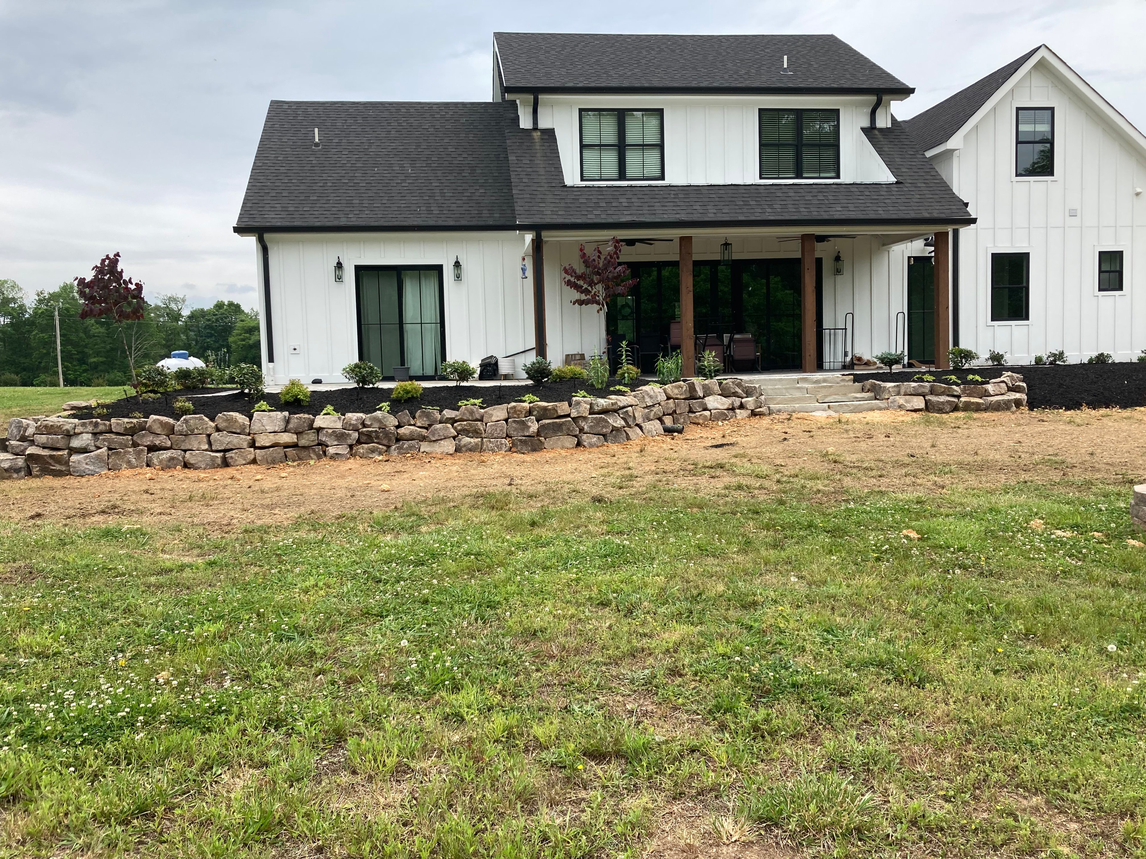 Modern farmhouse with stone retaining wall and garden beds